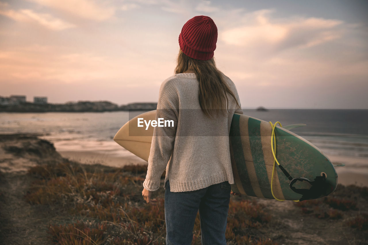 Rear view of woman carrying surfboard at beach