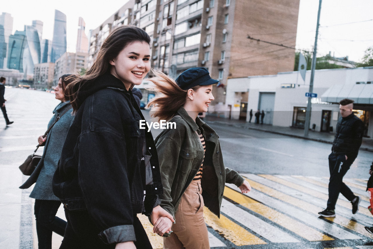 Smiling friends walking on road in city