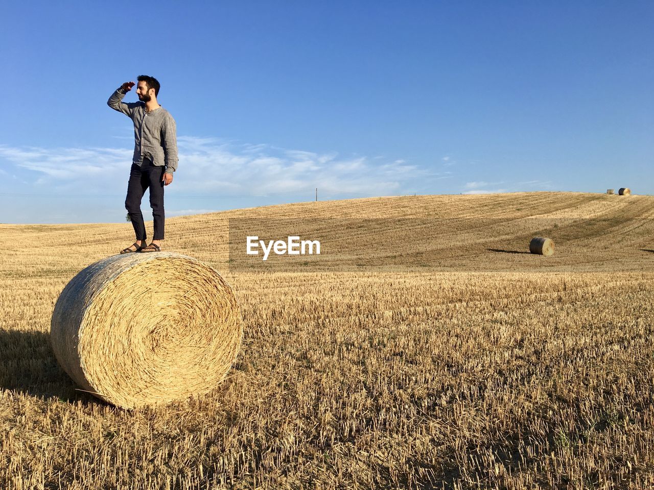 Man with hay bales on field against sky