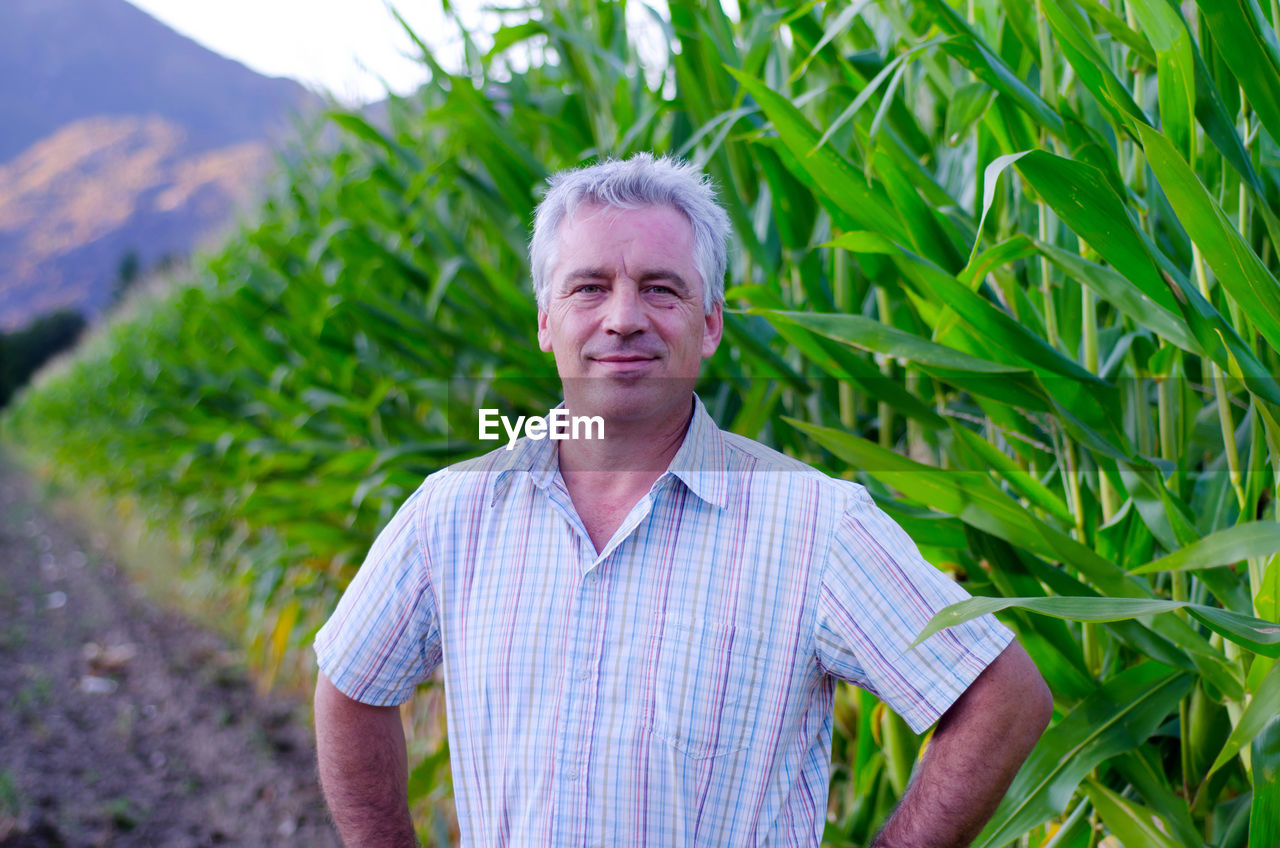 Portrait of smiling mature farmer standing against plants