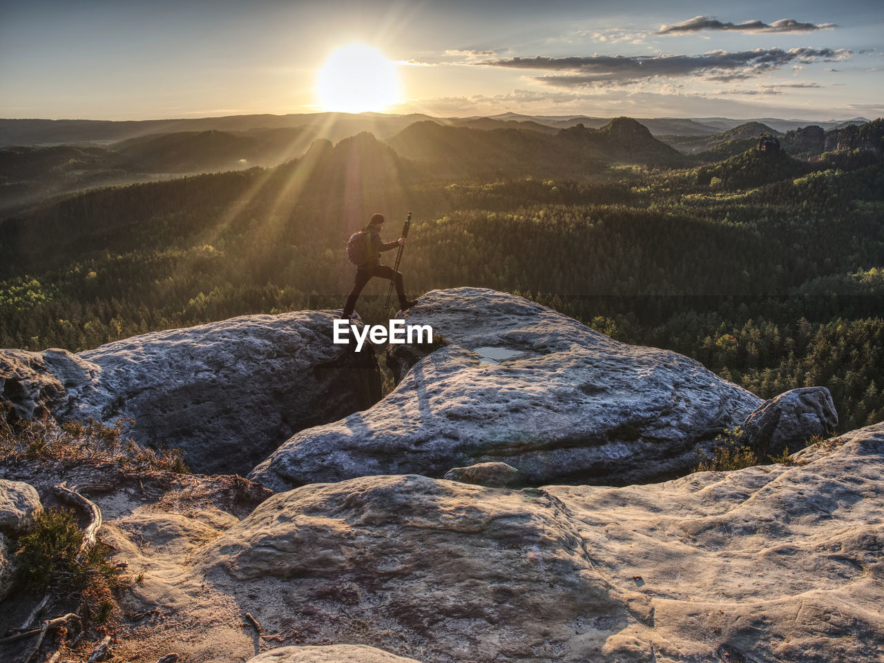 Photographer on mountain cliff above valley with morning mist hold tripod . hiker will take picture