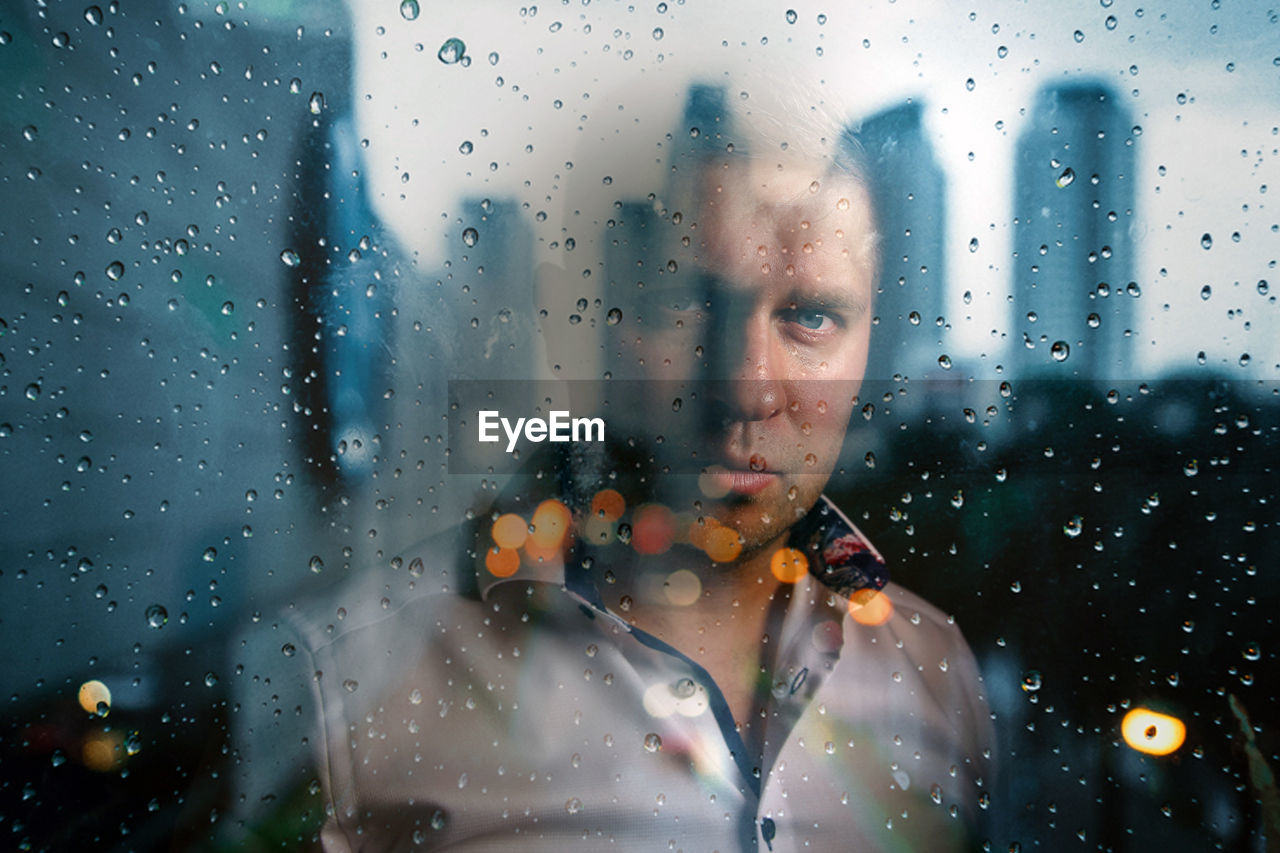 Portrait of man looking through wet glass window in rainy season