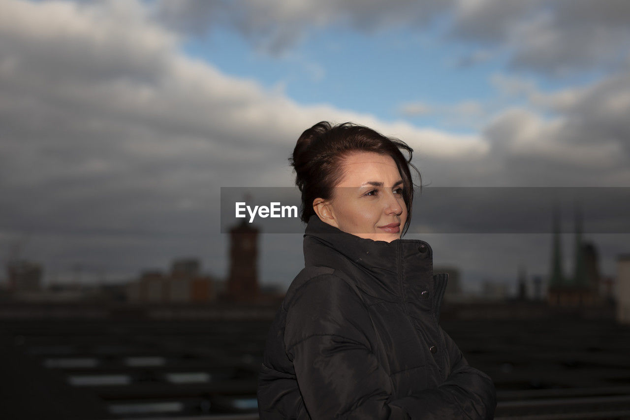 portrait of young woman looking away against sky during sunset