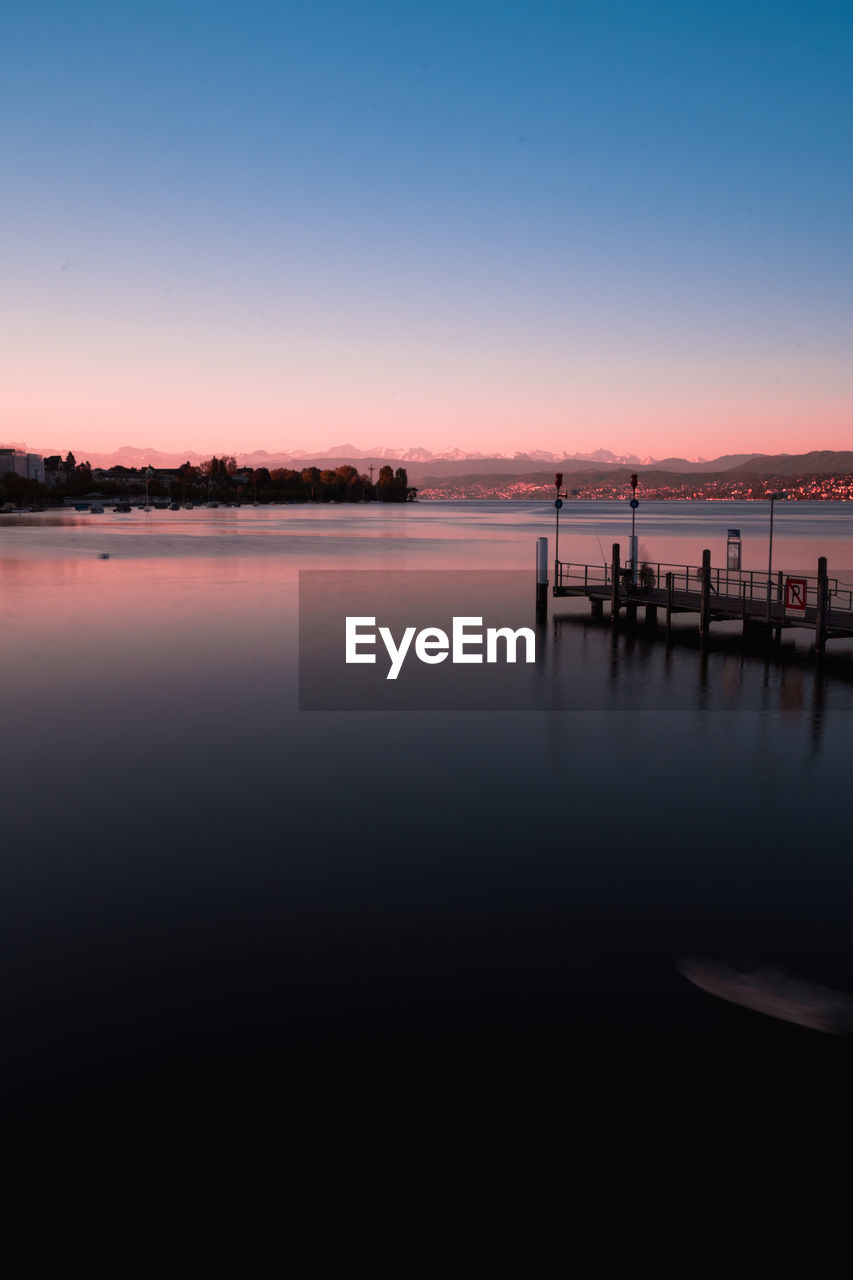 SILHOUETTE WOODEN POSTS IN LAKE AGAINST SKY DURING SUNSET