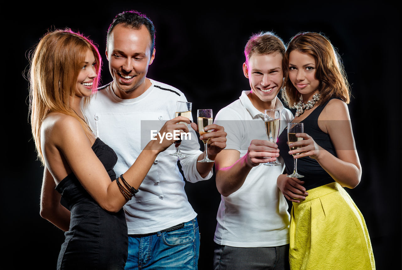 Friends holding champagne flutes while standing against black background