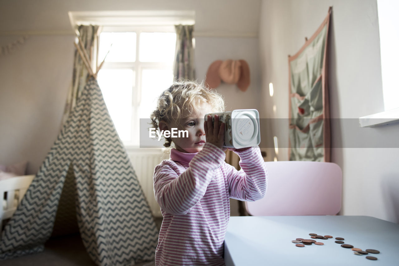 Girl looking in piggy bank while standing by table at home