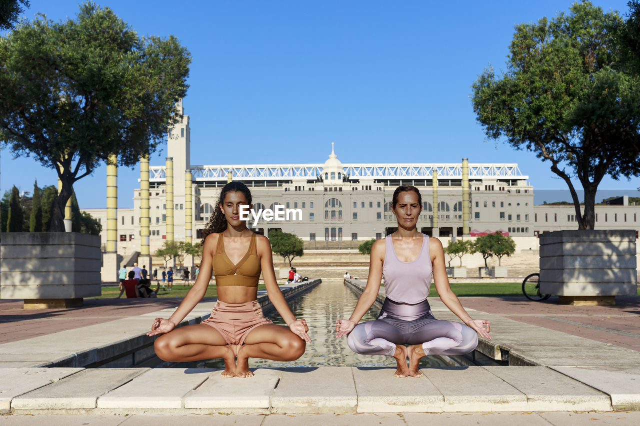 Teenage girl doing yoga with mother by water basin