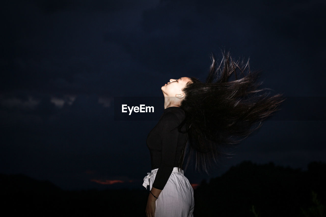 Side view of woman tossing hair standing outdoors at night