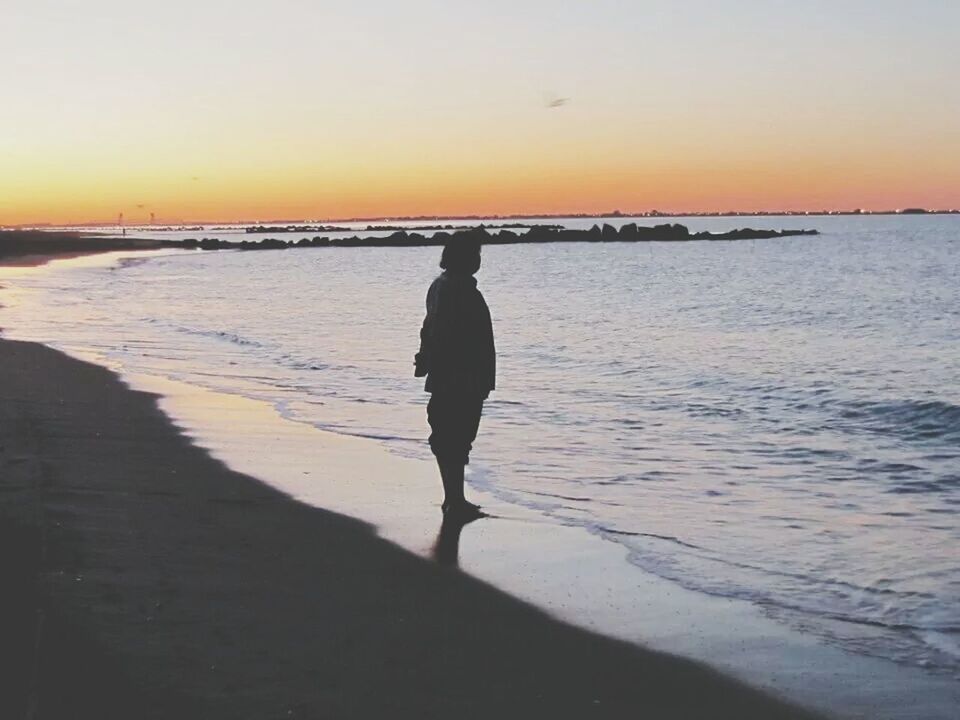 SILHOUETTE OF WOMAN STANDING ON BEACH AT SUNSET