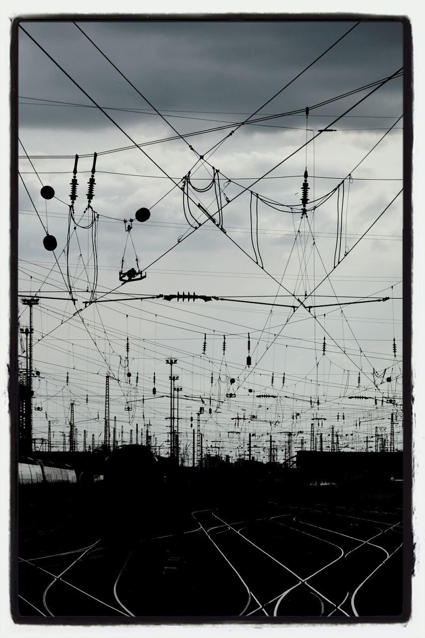 Railroad tracks and electricity pylons against cloudy sky