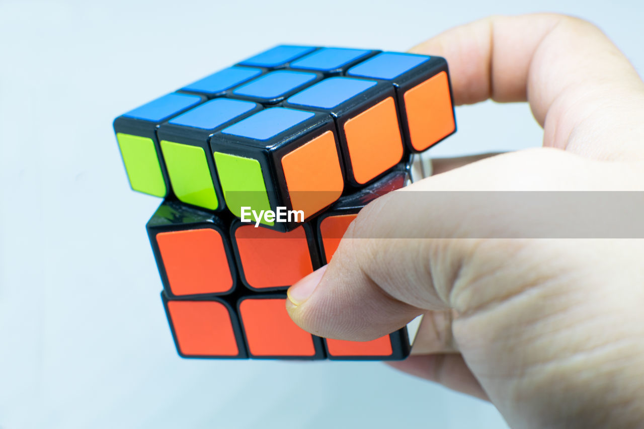 rubik's cube, hand, toy, puzzle, mechanical puzzle, holding, cube shape, close-up, one person, toy block, studio shot, indoors, shape, business, block shape, block, geometric shape, leisure activity, adult