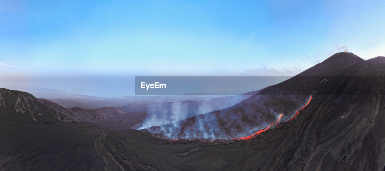 Etna erupting top view with lava flow and smoke-blue sky during blue hour- aerial panorama at sunset