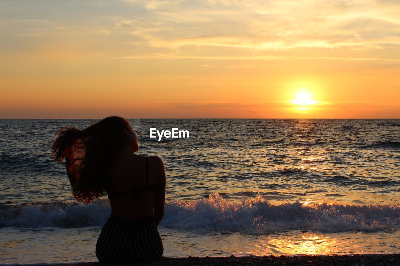 Silhouette woman looking at sea against sky during sunset