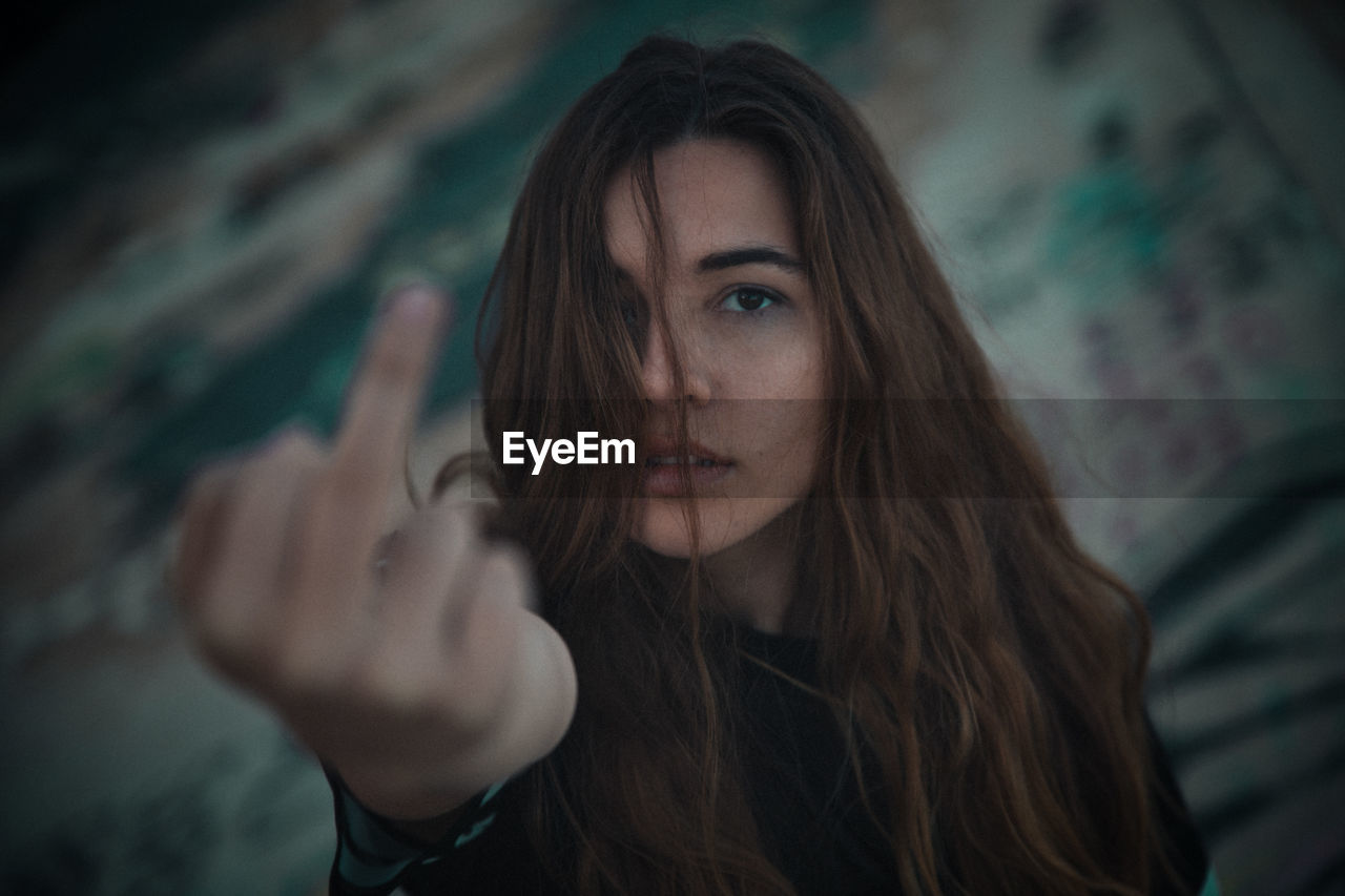 Close-up portrait of young woman making obscene gesture