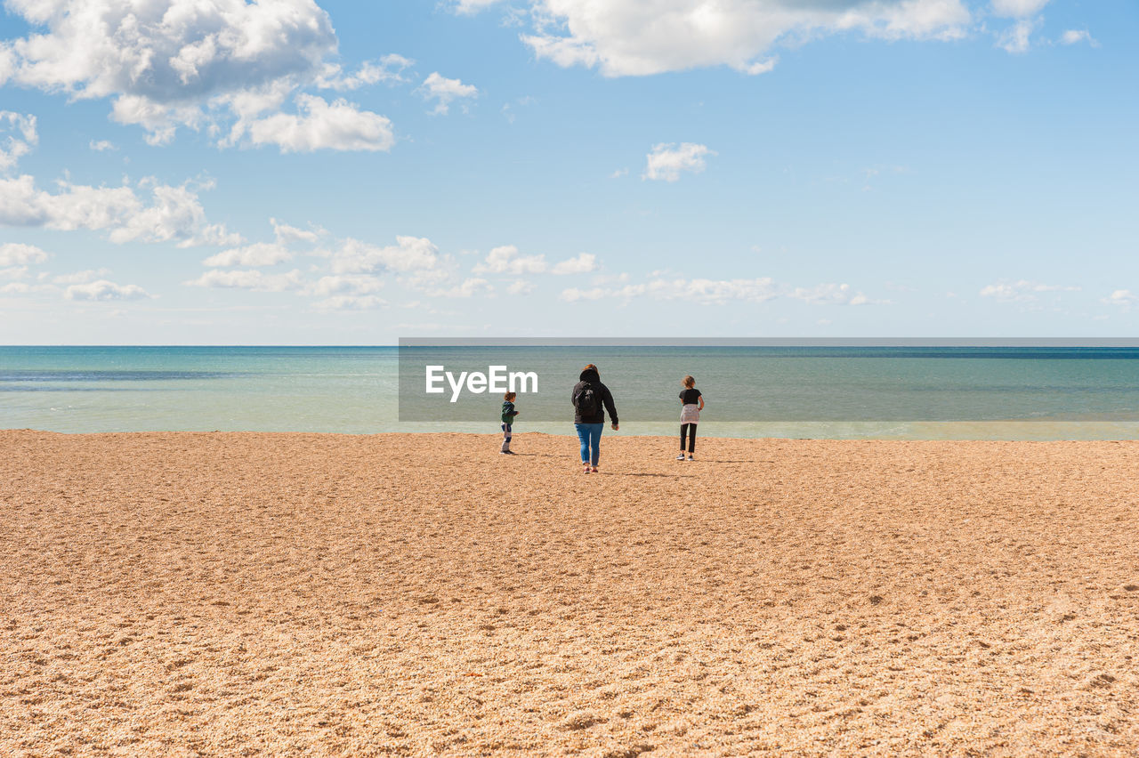 Rear view of mother and kids standing on beach against sky