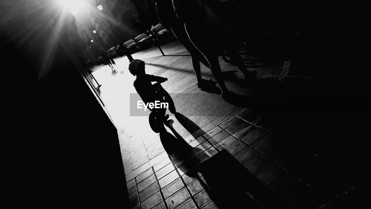 Silhouette child riding bicycle on sidewalk