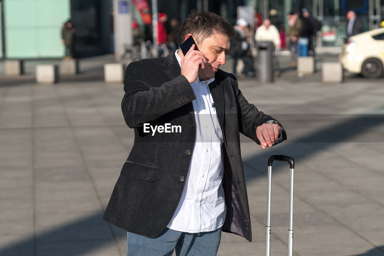 Man talking on mobile phone while checking time in city