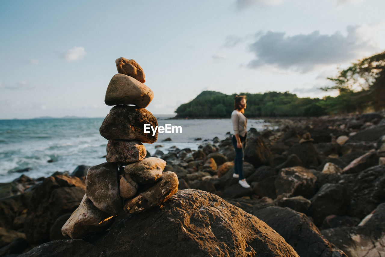 Stacked rocks at beach with woman standing in background during sunset