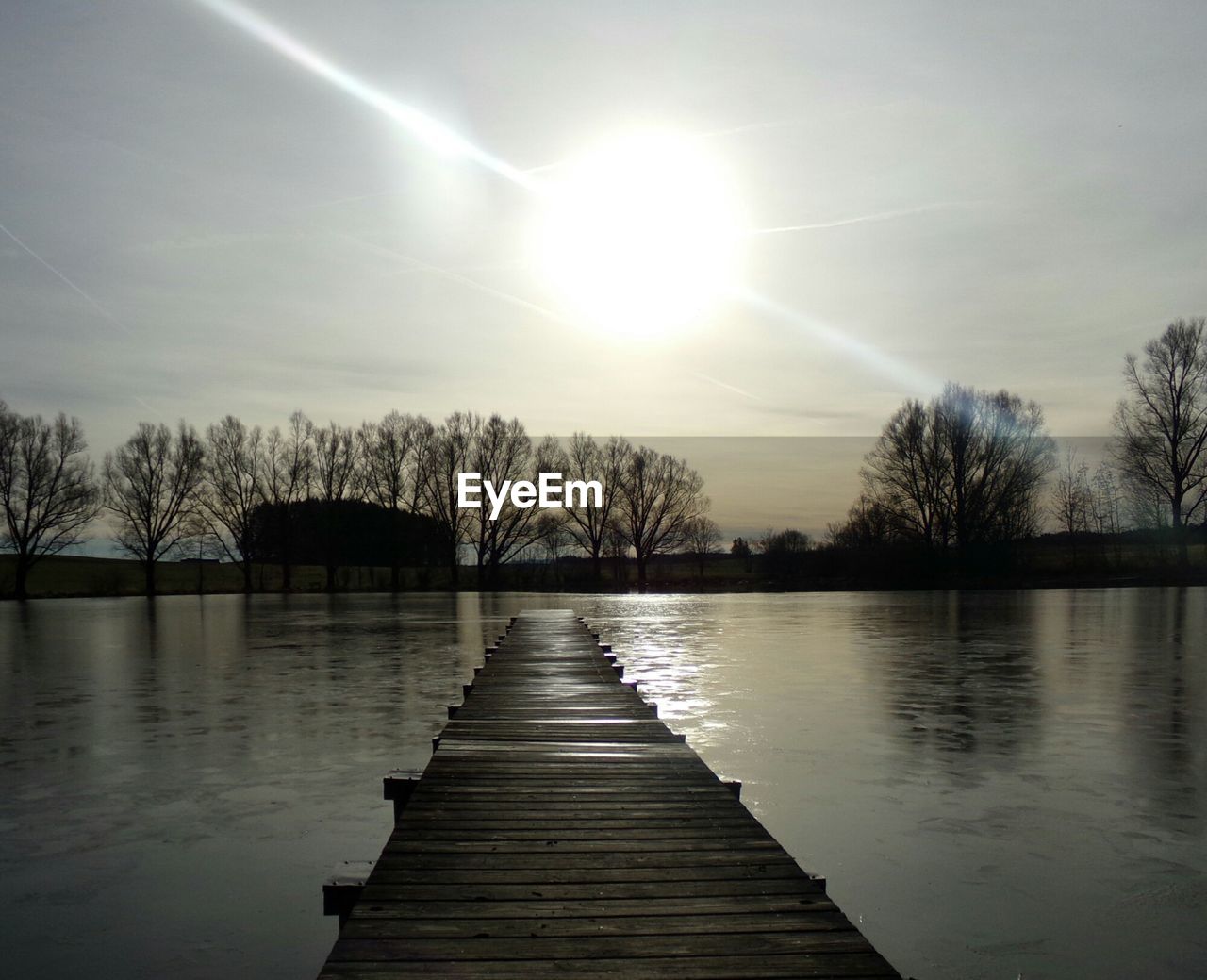 Empty pier over lake against sky on sunny day