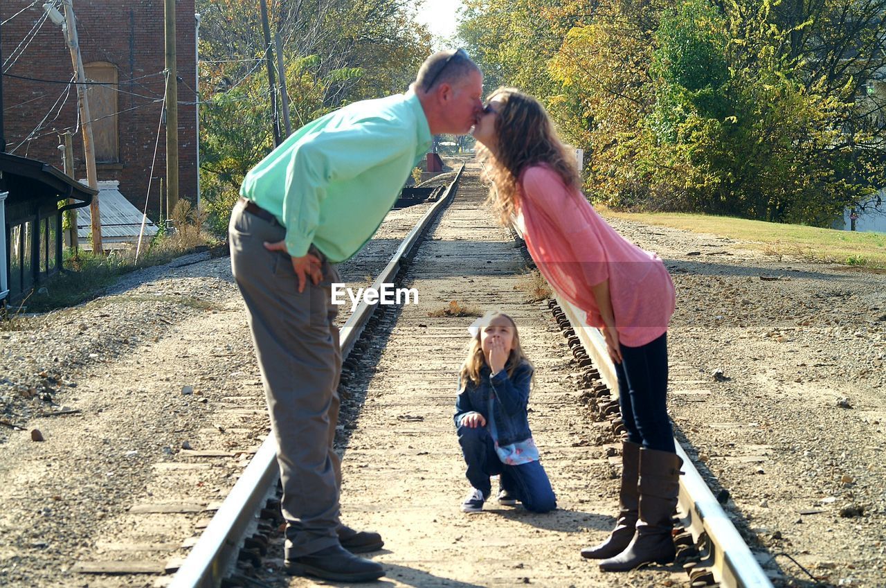 Girl looking at parents kissing on railroad track
