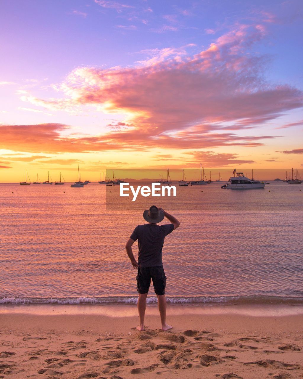 Rear view of man standing at beach against sky during sunset