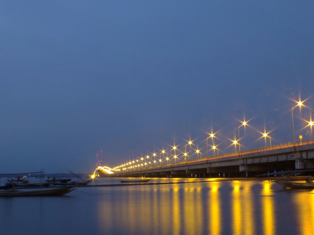 Low angle view of illuminated suramadu bridge over river against clear sky at dusk