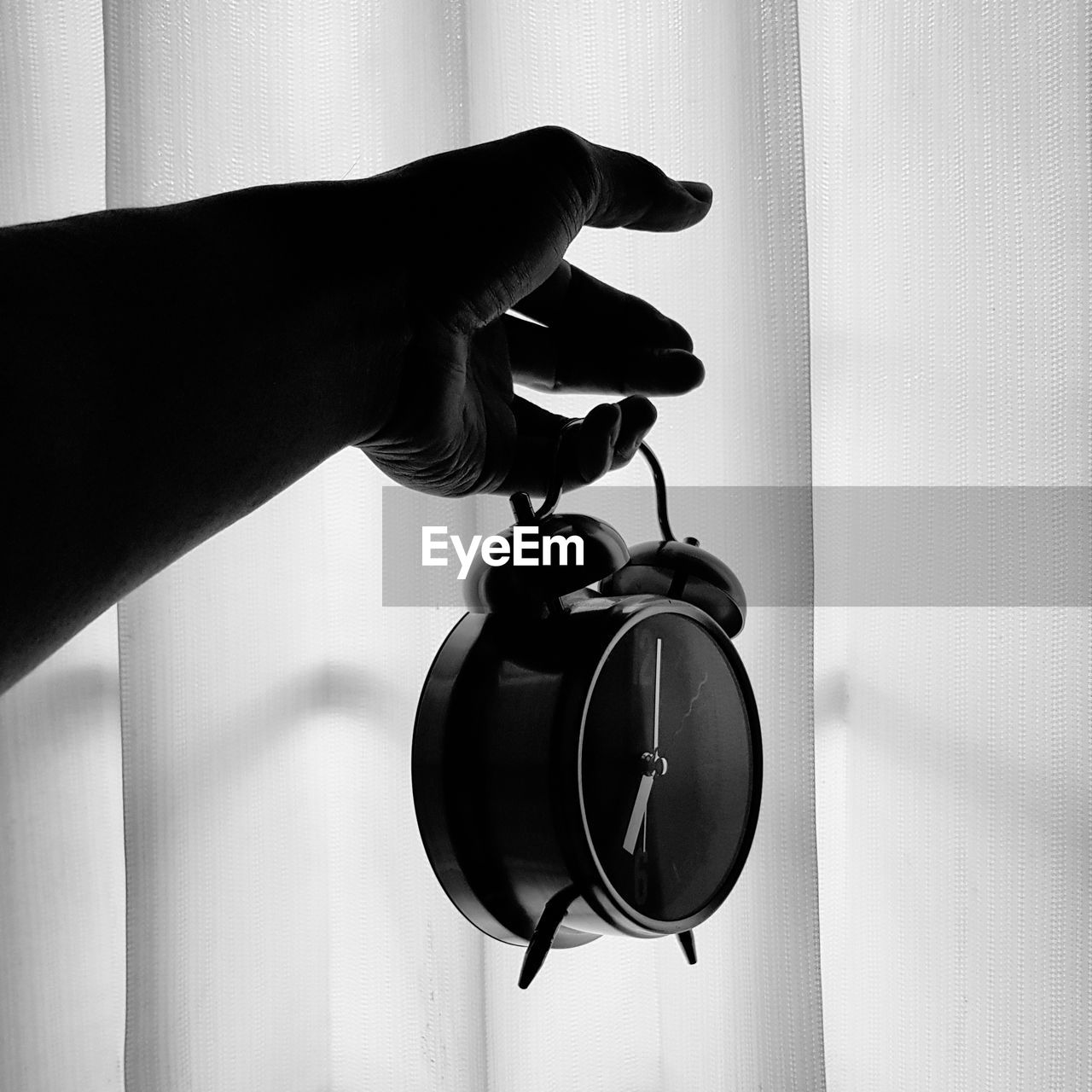 Close up of human hand holding alarm clock against curtain