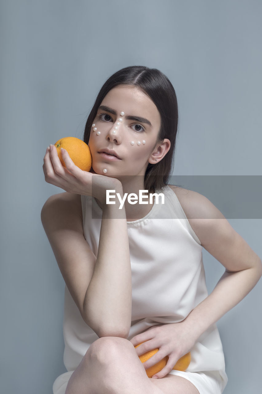 Young woman holding orange fruit against blue background