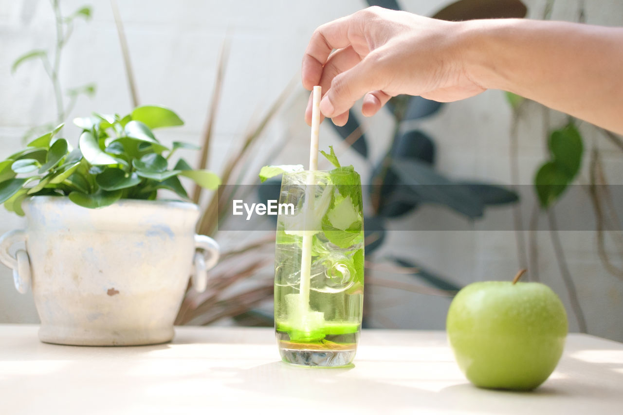 CROPPED IMAGE OF HAND HOLDING DRINK WITH GLASS OF TABLE