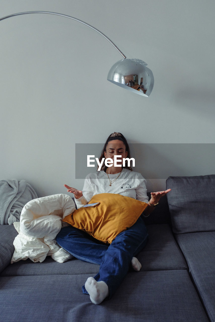 Smiling young woman meditating while sitting on sofa at home