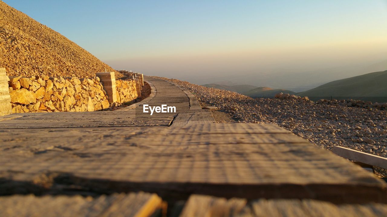 Wooden walkway by mountains against sky