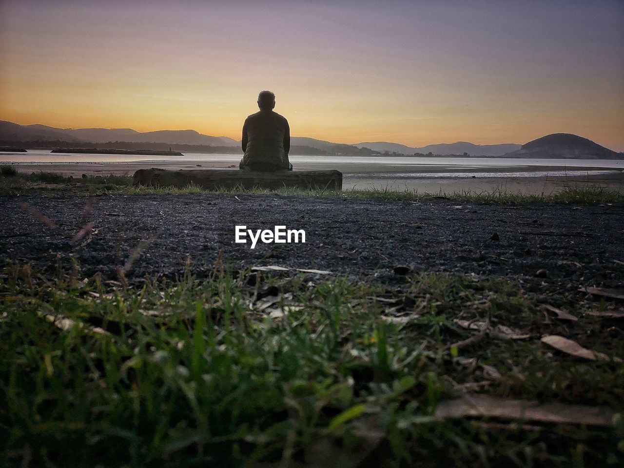 REAR VIEW OF MAN STANDING ON FIELD AT SUNSET