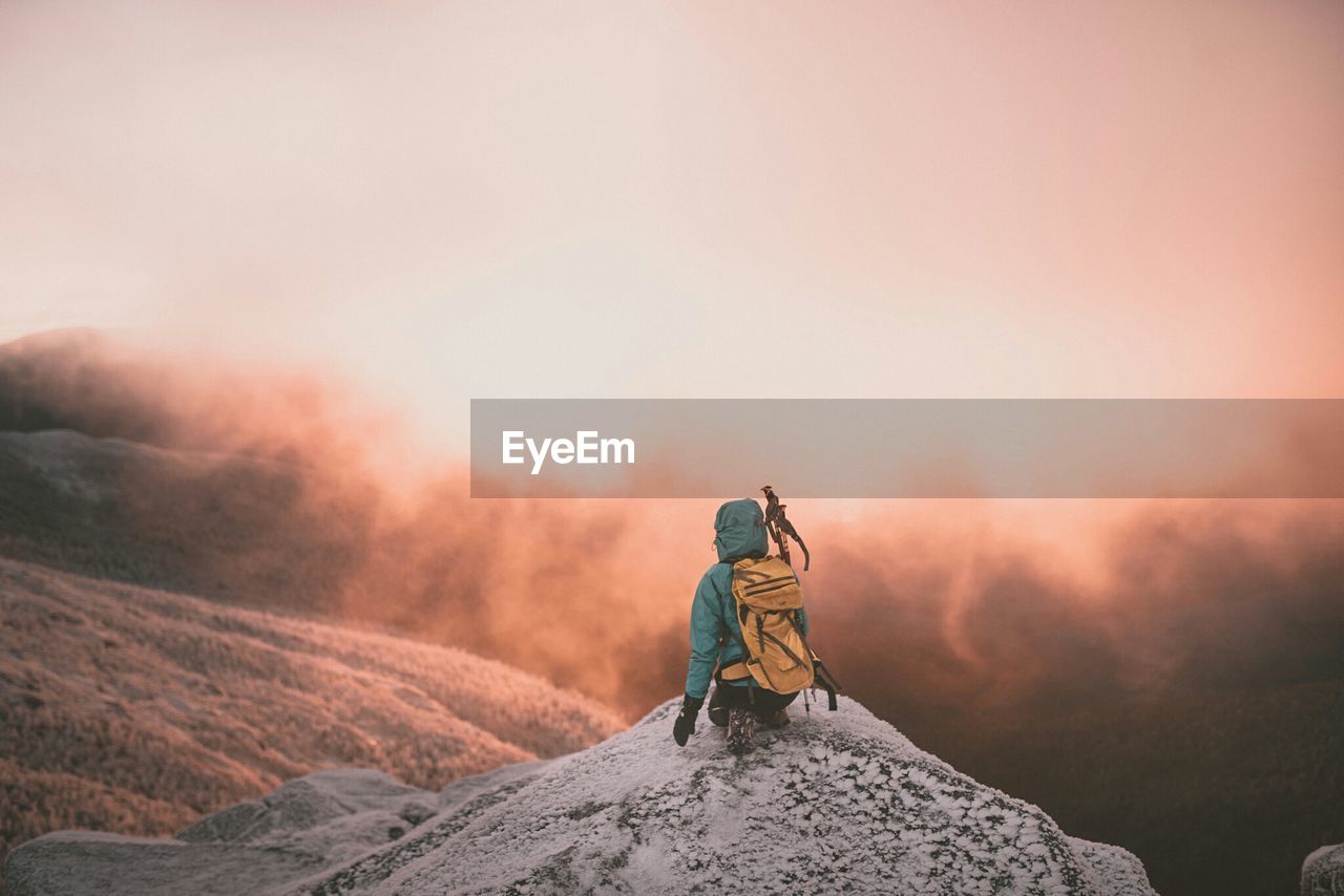 Rear view of hiker on mountain peak against cloudy sky during sunrise