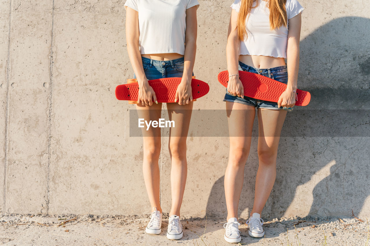 Two girls in white t-shirts and denim shorts holding skateboard