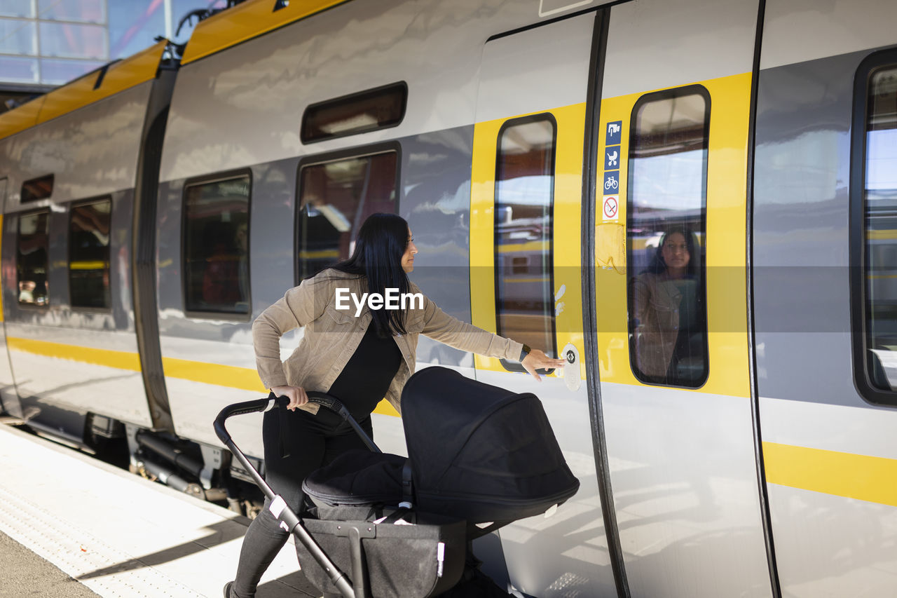 Mid adult woman at train station with pram opening train door