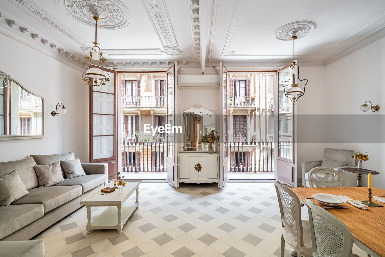 Front view to retro style living room, with dining table, sofa, vintage chandeliers and balconies