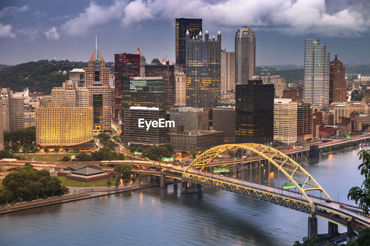 Bridge over river by buildings against sky in city