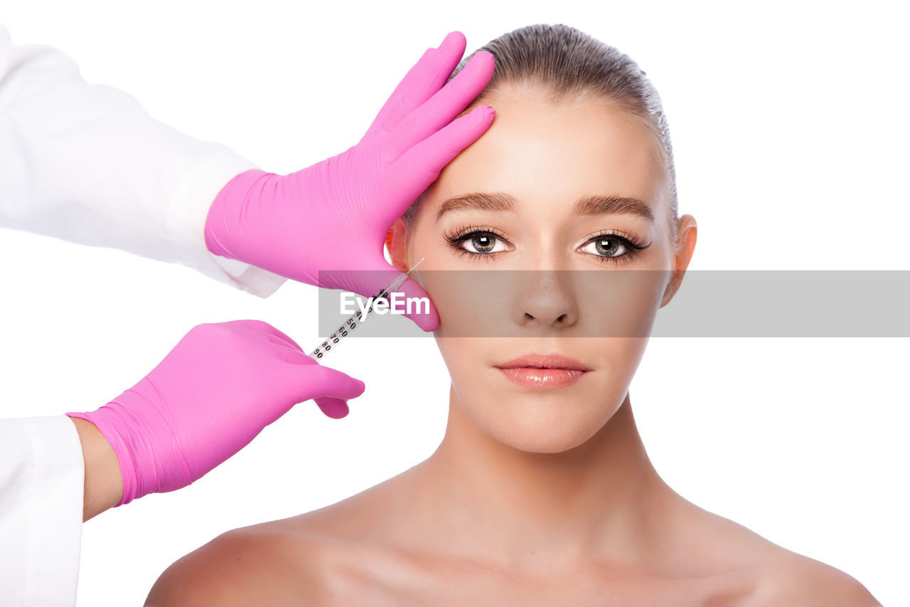 Cropped hands of surgeon giving botox injection to woman against white background