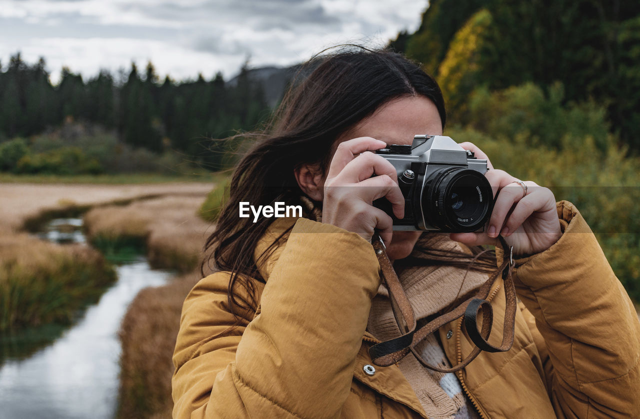 Portrait of young woman taking photos of beautiful autumn nature with a vintage film