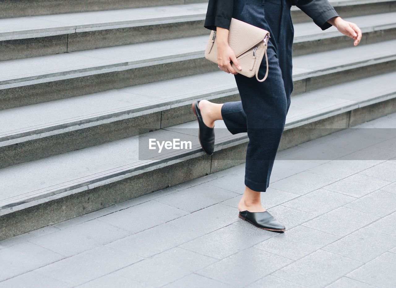 Low section of woman holding purse while moving down on steps