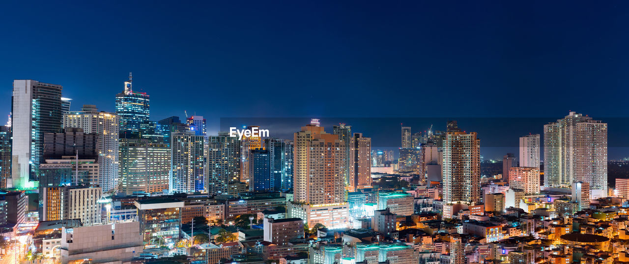 Illuminated buildings in city against blue sky