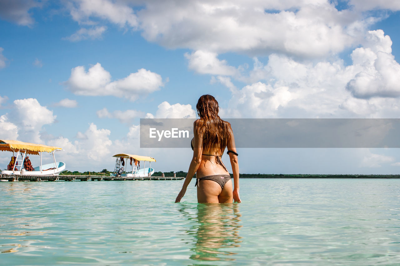 REAR VIEW OF WOMAN WITH ARMS RAISED STANDING AT BEACH