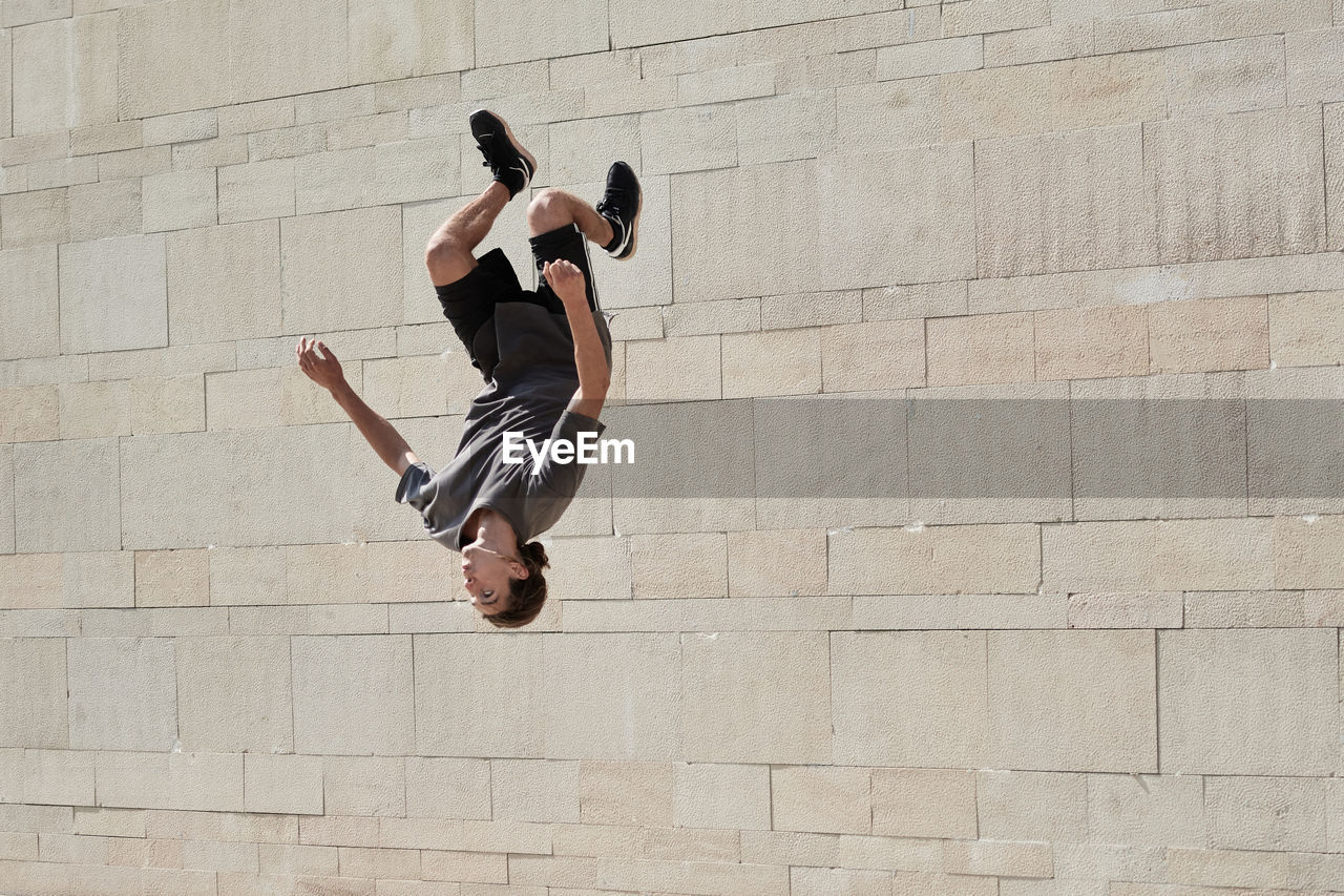 Upside down of young male doing somersault while practicing parkour in urban area in summer