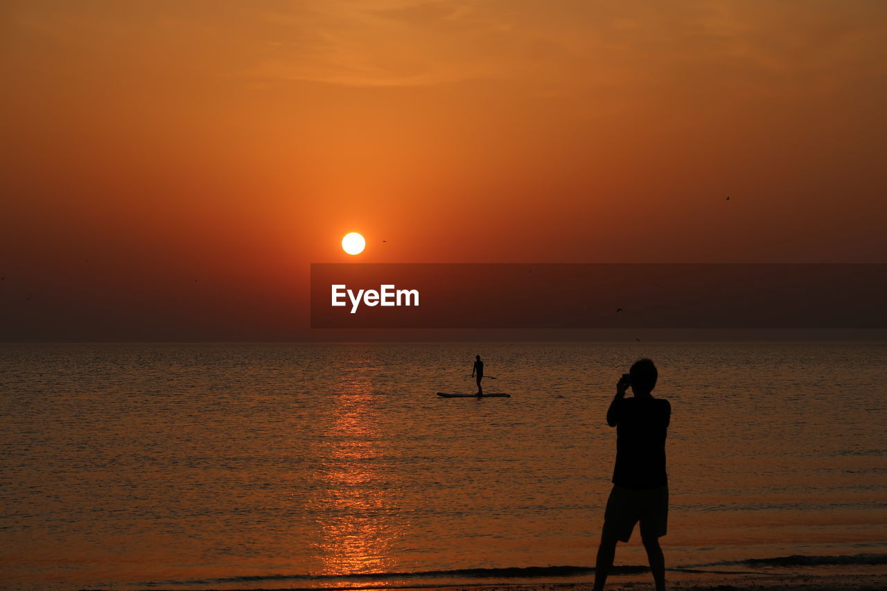 SILHOUETTE PEOPLE ON BEACH AGAINST ORANGE SKY