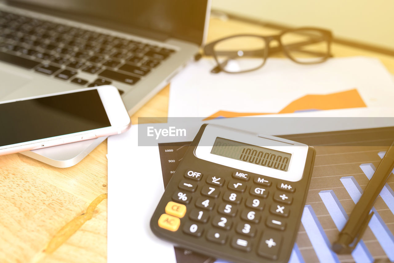 Close-up of calculator by smart phone and laptop over documents on table