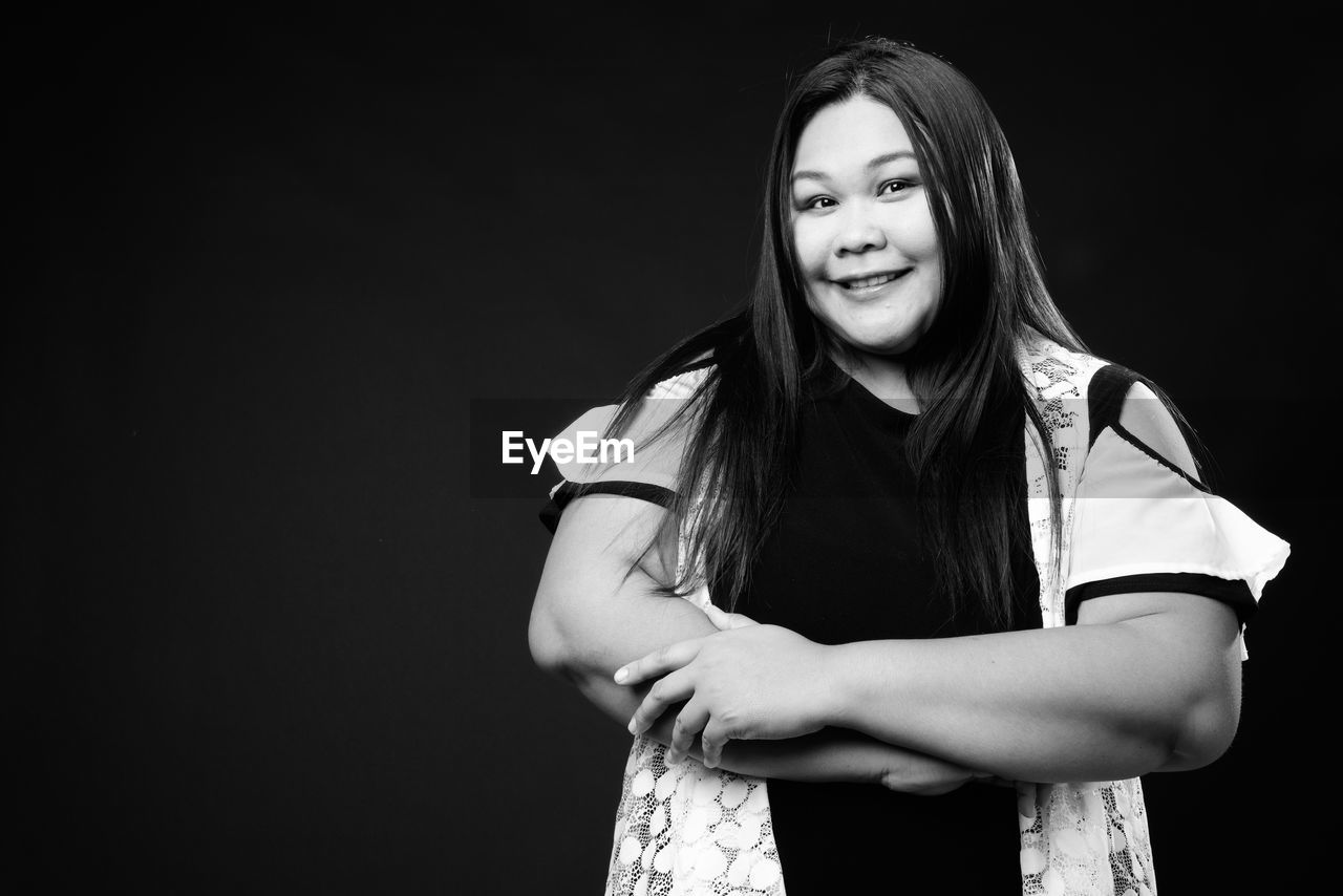 Portrait of smiling young woman against black background