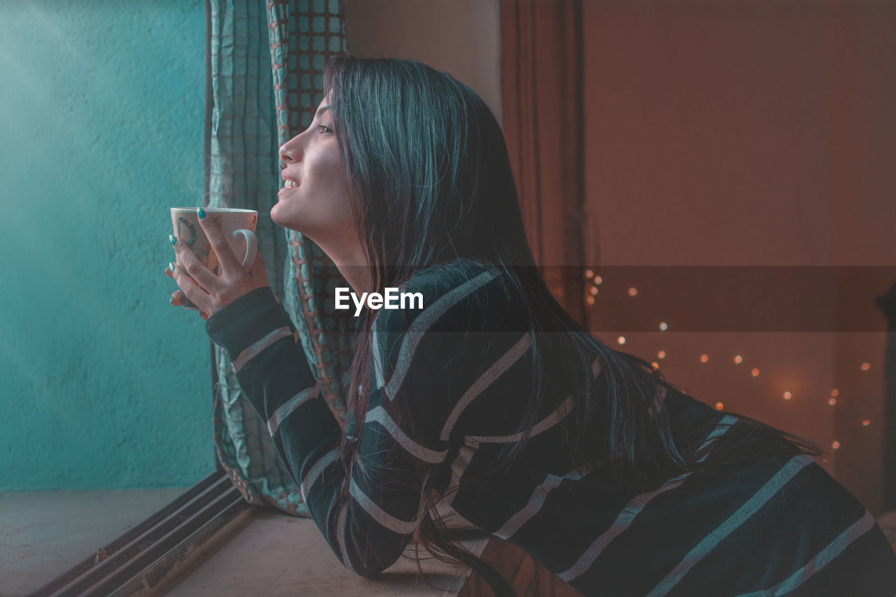 SIDE VIEW OF YOUNG WOMAN DRINKING COFFEE CUP