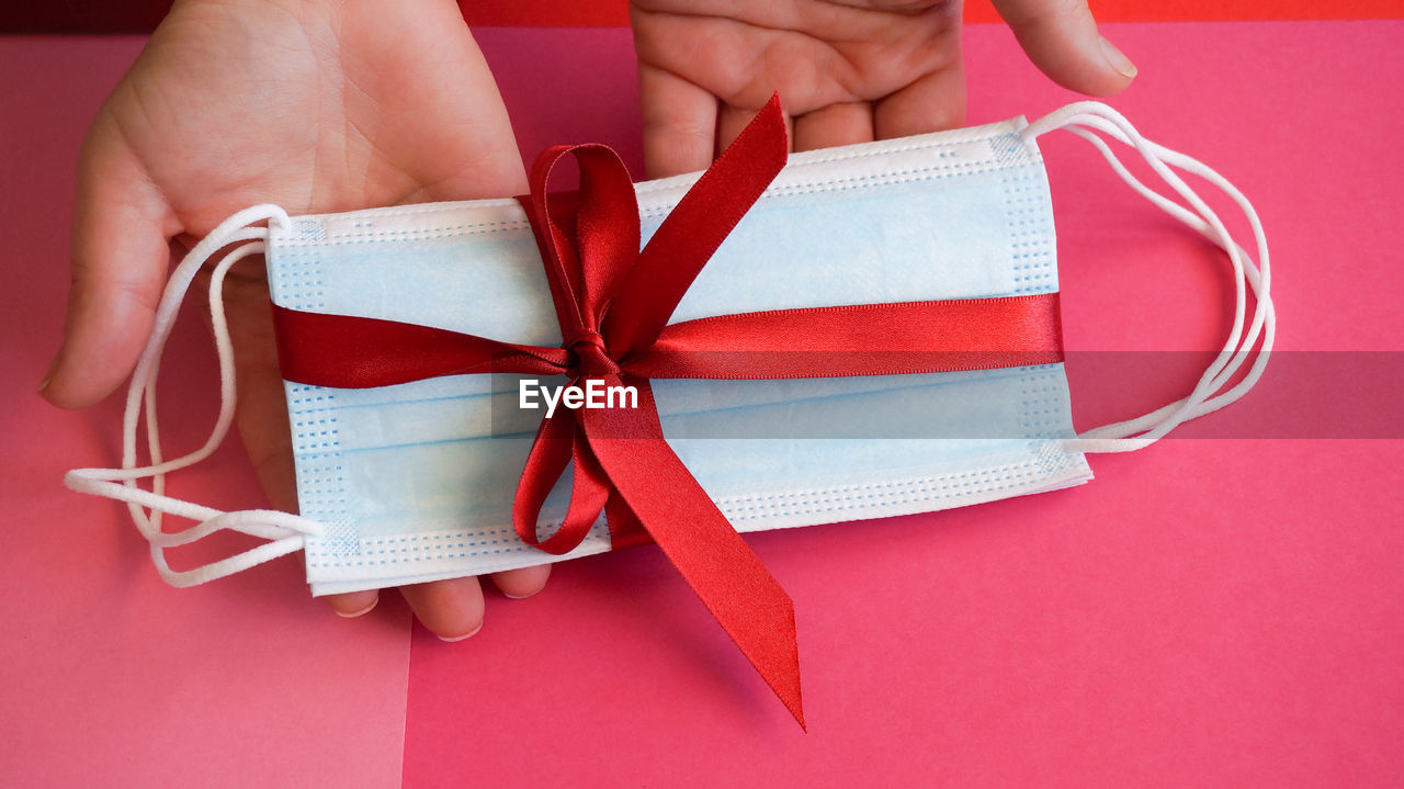 Medical face masks with red ribbon in hands as a present 