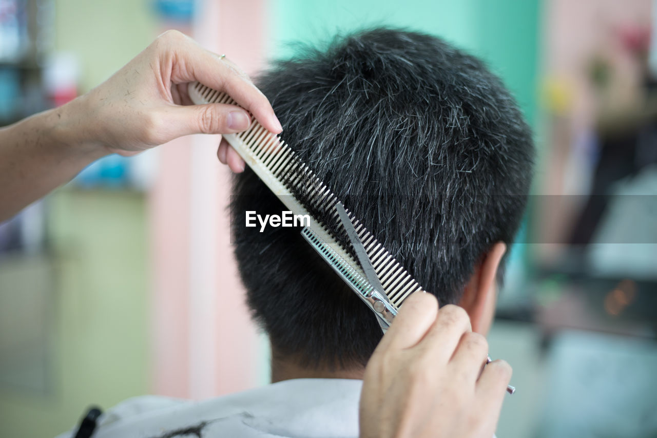 Close-up of barber cutting hair of man at shop