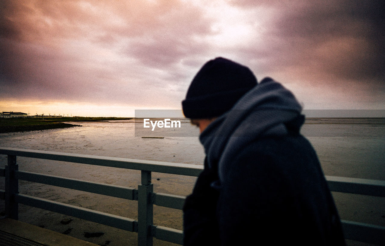 REAR VIEW OF BOY STANDING BY SEA AGAINST SKY